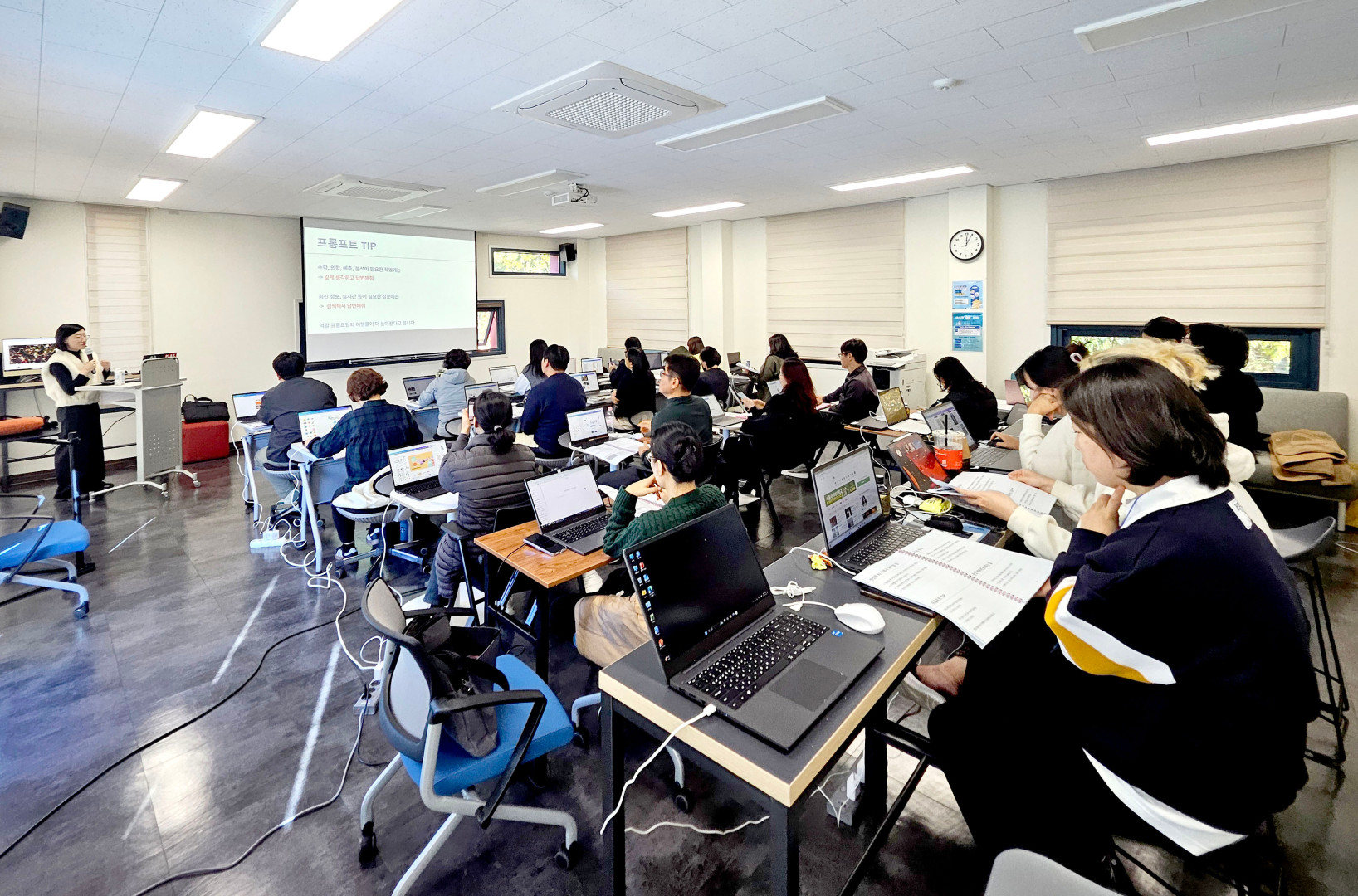 포항대학교 강의실에서 진행 중인 프롬프트 활용 교육 현장 사진. 화면 앞쪽 스크린에는 '프롬프트 TIP'이라는 제목과 함께 '수학, 의학, 예측, 분석이 필요한 작업에는 깊게 생각하고 답변해줘', '최신 정보, 실시간 등이 필요한 질문에는 검색해서 답변해줘' 등의 상세 내용이 띄워져 있습니다. 강사가 스크린 앞에서 마이크를 들고 설명하고 있으며, 약 20여 명의 교육생이 각자 노트북을 펼쳐 실습에 집중하고 있는 뒷모습이 담겨 있습니다.