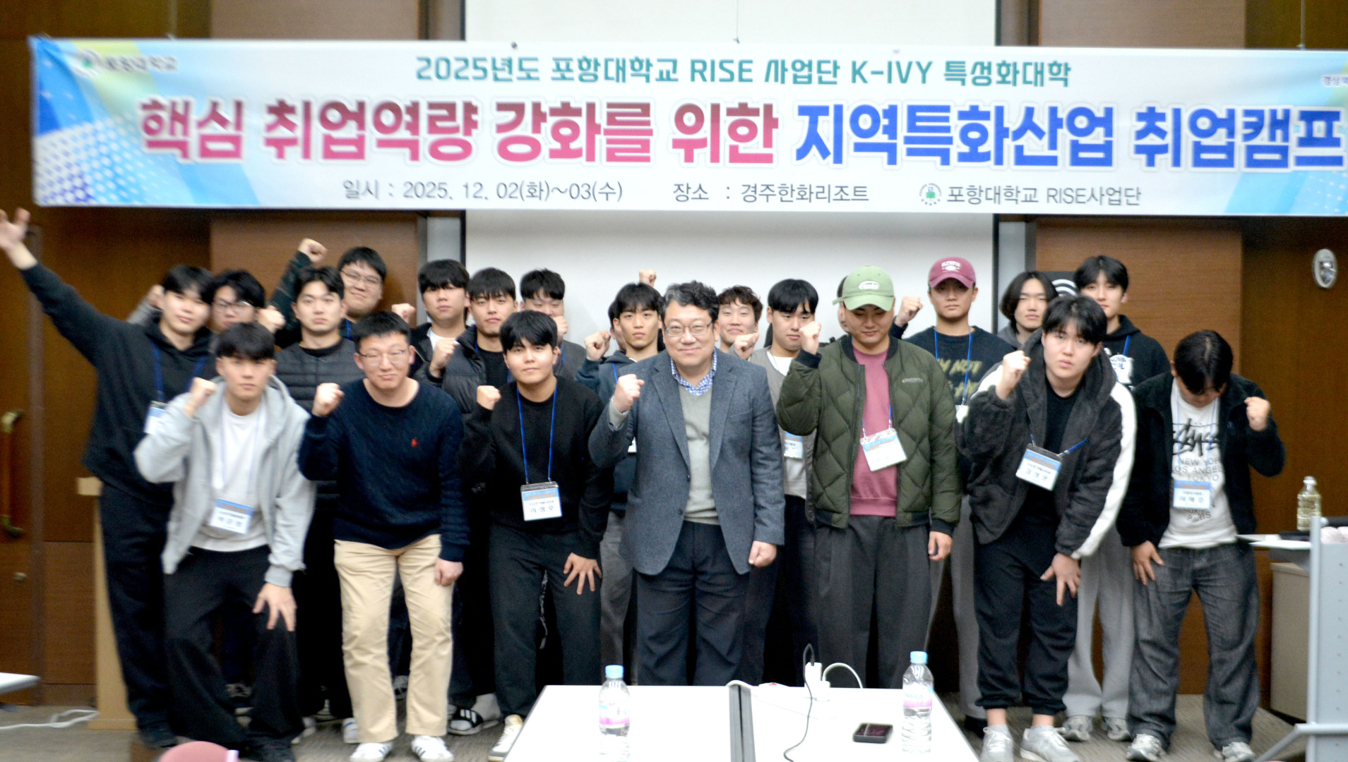 2025년도 포항대학교 RISE 사업단 K-IVY 특성화대학 핵심 취업역량 강화를 위한 지역특화산업 취업캠프 단체 기념사진. 상단 현수막 정보: 일시 2025.12.02(화)~03(수), 장소 경주한화리조트, 주최 포항대학교 RISE 사업단. 세미나실 현수막 아래로 약 20여 명의 남성 학생들이 모여 있으며, 중앙의 지도 교수와 학생들이 함께 오른쪽 주먹을 쥐고 파이팅 포즈를 취하며 정면을 바라보고 있습니다.